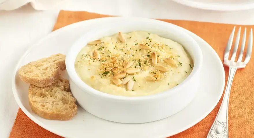 Deliciosa brandada de merluza cremosa, gratinada con piñones y pan rallado, servida con tostas.