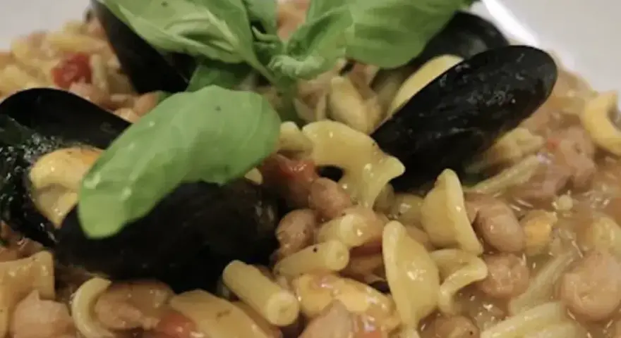 Un piatto invitante di pasta fagioli e cozze, guarnito con foglie di basilico fresco.