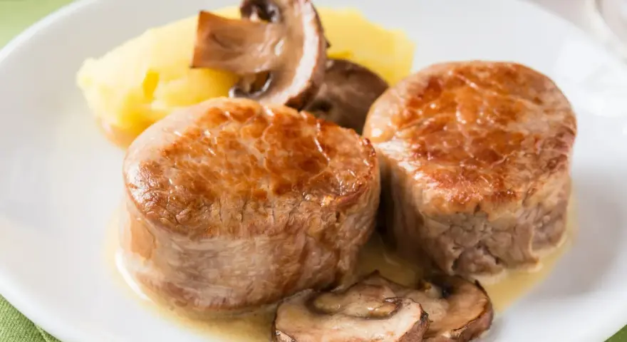 Dwie soczyste polędwice wieprzowe podane z puree ziemniaczanym i pieczarkami w sosie.