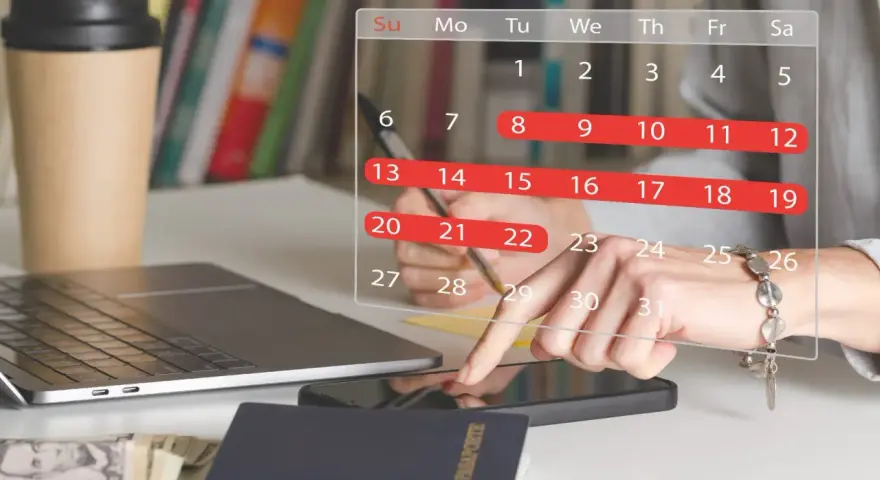 Planowanie urlopu zgodnie z kodeksem pracy. Na biurku laptop, paszport, pieniądze i kalendarz z zaznaczonymi dniami.