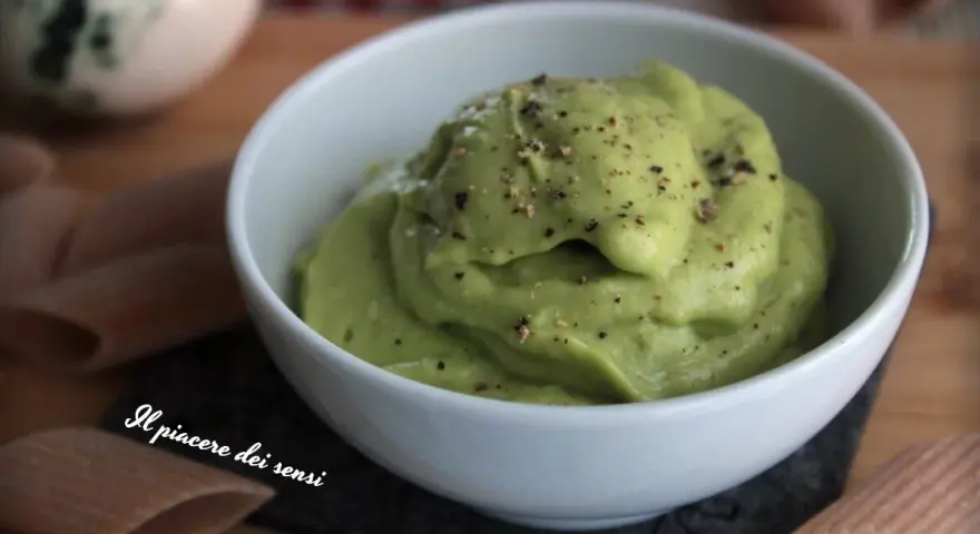 Una ciotola bianca piena di vellutata crema di avocado, cosparsa di pepe nero macinato. Accanto, pasta integrale.