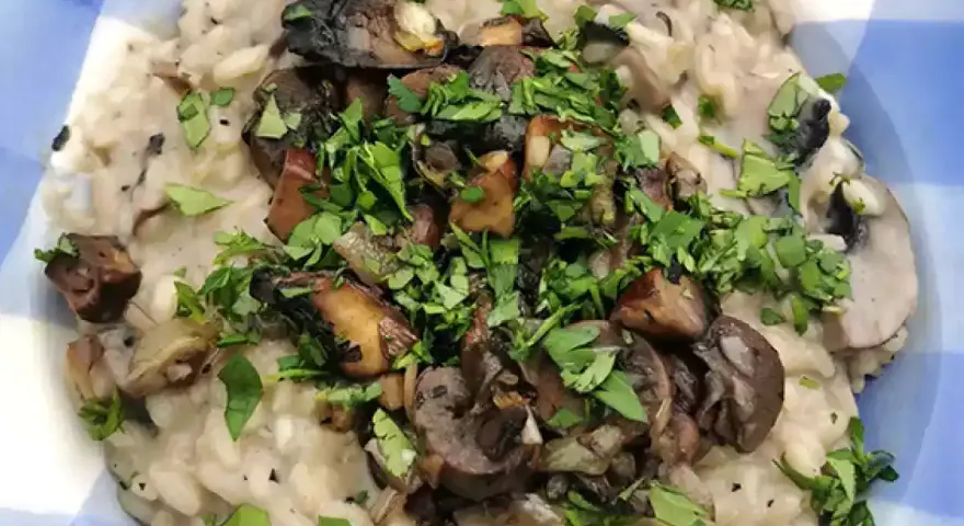 Risotto cremoso con champiñones salteados y perejil picado en un plato azul a cuadros.