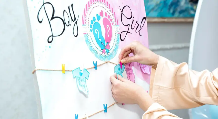 Ręce wieszają ozdoby na przyjęciu z okazji baby shower, kiedy płeć dziecka jest pewna. Napisy "Boy" i "Girl" oraz dziecięce ubranka.