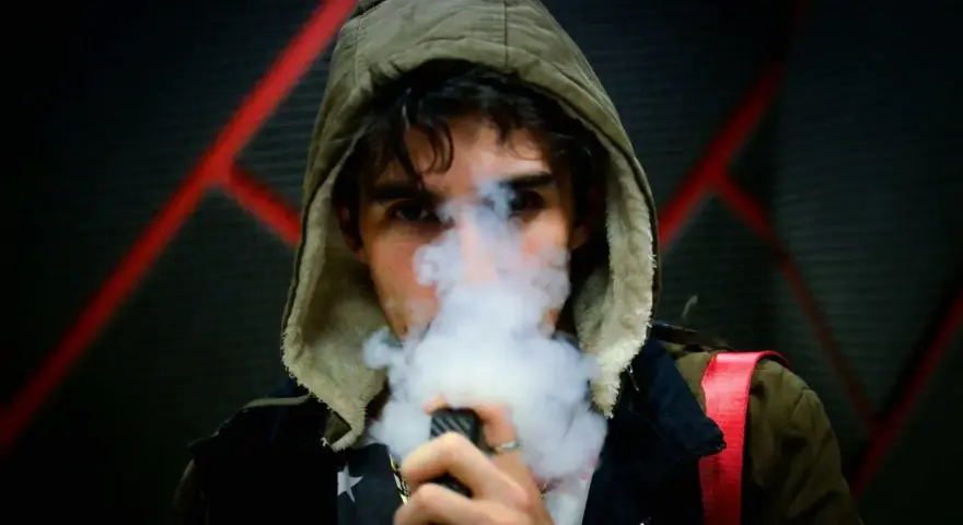 Joven con capucha exhala vapor de un vapeador, con un diseño de estrellas en su camiseta. Los nicokits son su secreto.