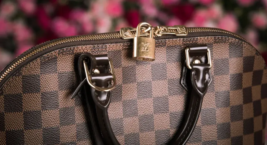 Dettaglio di una borsa Louis Vuitton, icona dell'azienda, con il classico motivo a scacchiera e un lucchetto dorato.