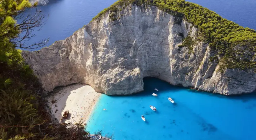 Widok na zatokę Navagio na Zakynthos z plażą, turkusową wodą i łodziami.