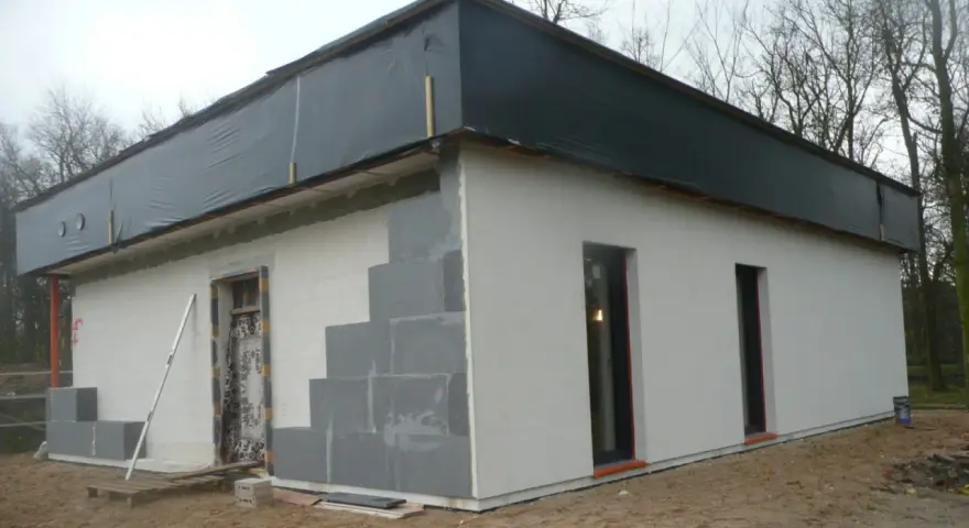 Budowa domu ze styropianu w trakcie. Widoczne bloczki, okna i dach przykryty czarną folią.