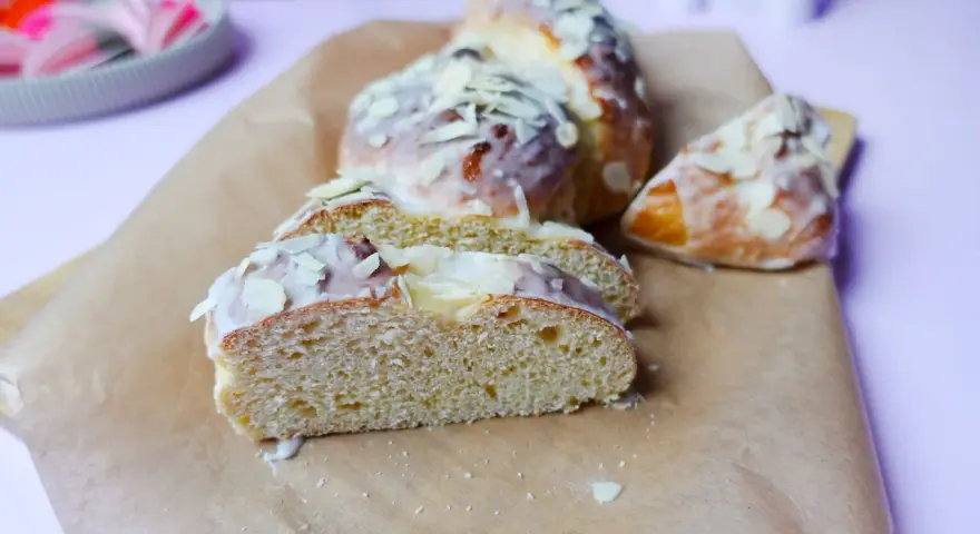 Süßer Hefekuchen ohne Zucker, mit zarter Glasur und Mandelblättchen bestreut, auf Backpapier angerichtet.