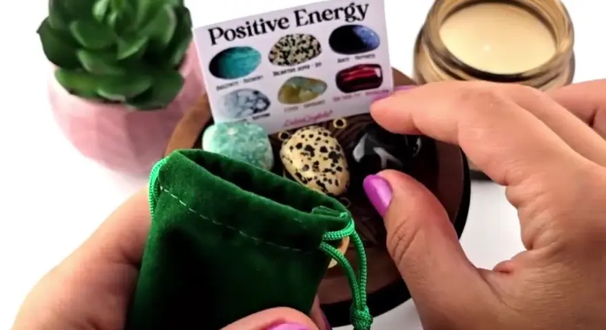 Manos sostienen una bolsa verde con piedras de energía positiva. Un folleto muestra varias piedras.