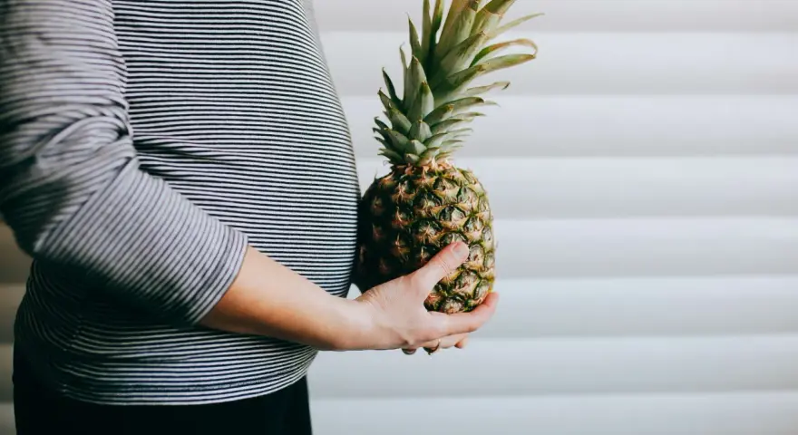 Brzuch kobiety w paski, trzymająca ananasa. Wygląda jak ananas w ciąży, symbolizujący zdrową dietę.