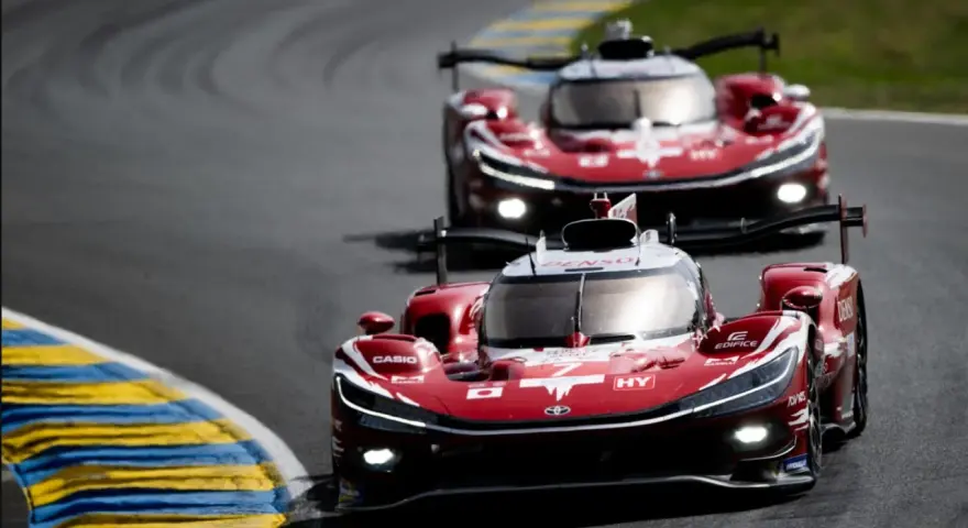Dos coches de carreras rojos compiten en Le Mans, sus luces brillan en la pista.