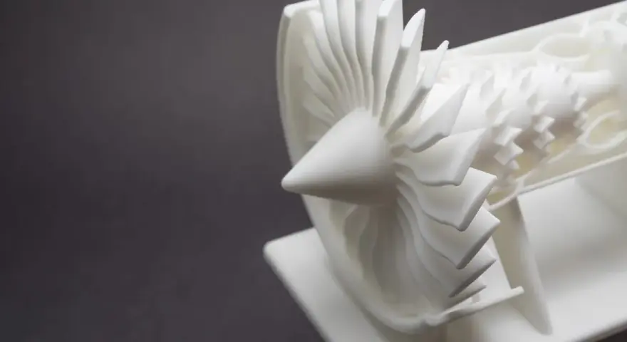 A detailed white model of a jet engine's turbine, showcasing intricate blades, likely created by a laser sintering machine.