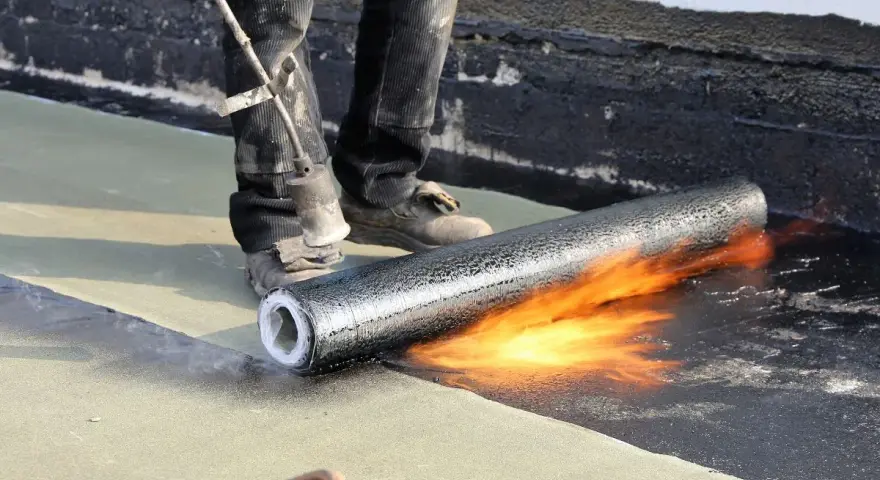 Application d'une membrane bitumineuse pour l'étanchéité d'une dalle béton extérieur. Un chalumeau chauffe le rouleau pour une pose parfaite.