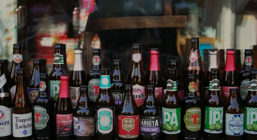 Rząd butelek z piwem kraftowym, w tym Trappistes Rochefort, Chimay, Goose Island i inne. Idealne na pytanie: jakie piwo kraftowe wybrać?