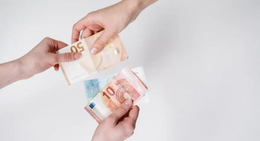 Dwie dłonie przekazują sobie banknoty euro. W Hiszpanii obowiązuje euro, więc to właśnie ta waluta jest tu widoczna.