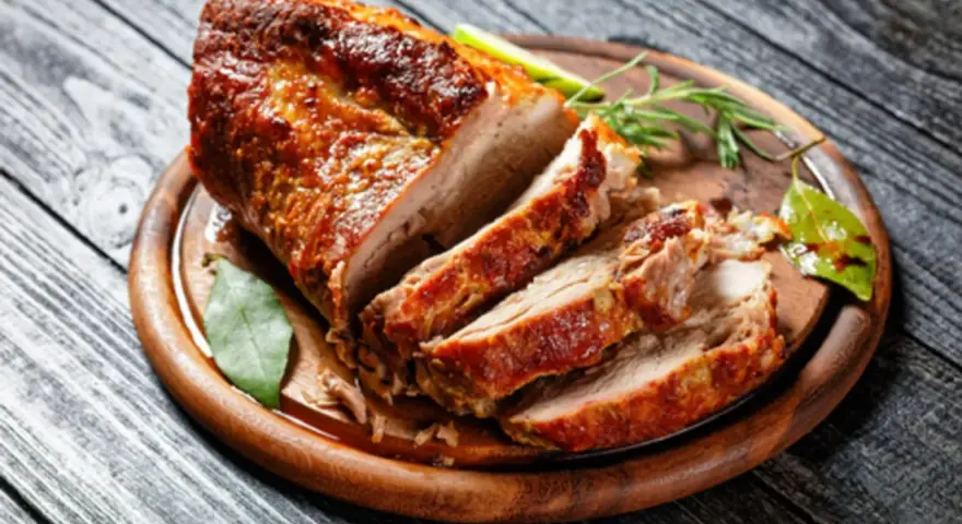 Un rôti de porc au four, coupé en tranches, sur une planche en bois. Le temps cuisson rôti de porc au four moelleux est parfait pour ce plat savoureux.