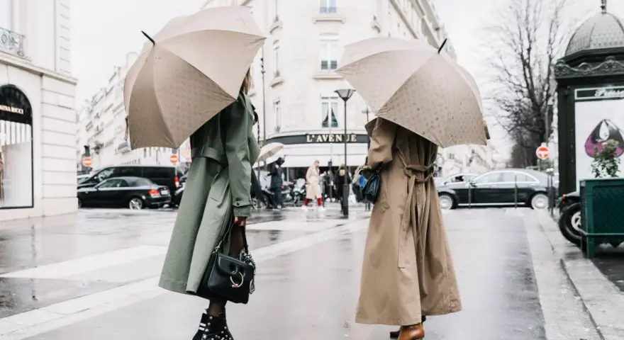 Dos mujeres con paraguas lucen elegantes gabardinas, como se llaman las chaquetas largas, en un día lluvioso en París.