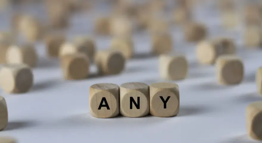 Holzwürfel mit den Buchstaben A, N, Y bilden das Wort "ANY". Sie liegen auf einem hellen Untergrund, umgeben von vielen weiteren unscharfen Würfeln.