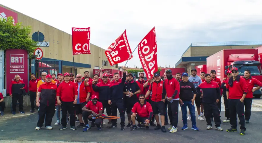 Un gruppo di lavoratori BRT, con bandiere rosse, manifesta per migliorare le condizioni di lavoro. Le loro opinioni su lavorare in Bartolini sono chiare.