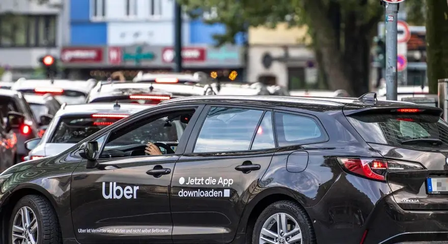 Ein dunkler Uber-Kombi steht im Stau. Die Aufforderung "Jetzt die App downloaden" ist gut sichtbar.
