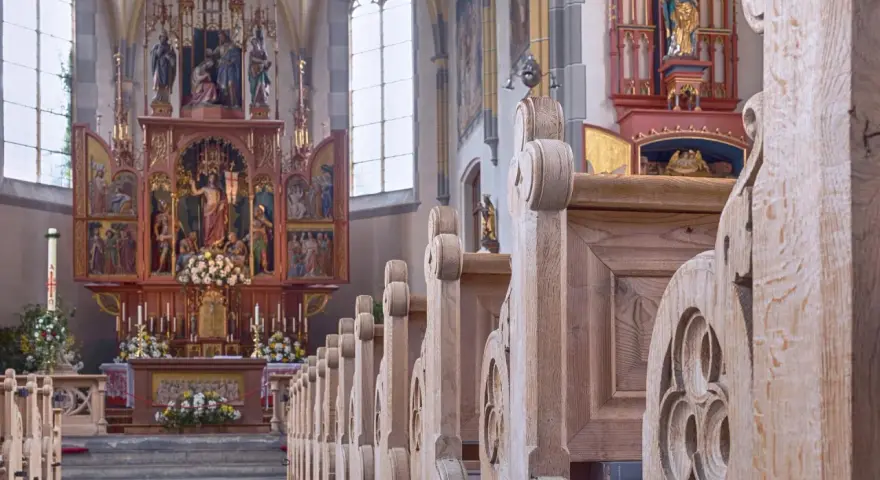 Drewniane ławki w kościele św. Jana w Warszawie, prowadzące do ołtarza z bogatymi zdobieniami i figurami.