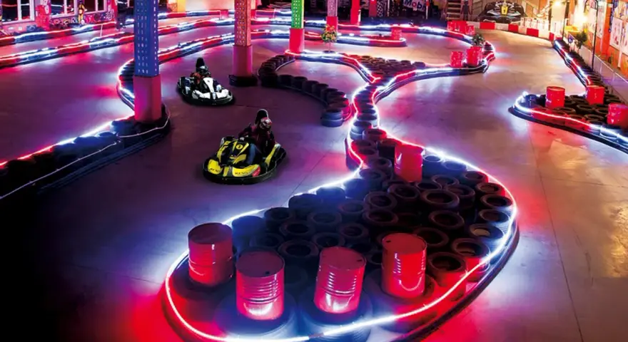 Tor kartingowy w stylu Canpol Wonderland, oświetlony neonami, z gokartami w akcji.