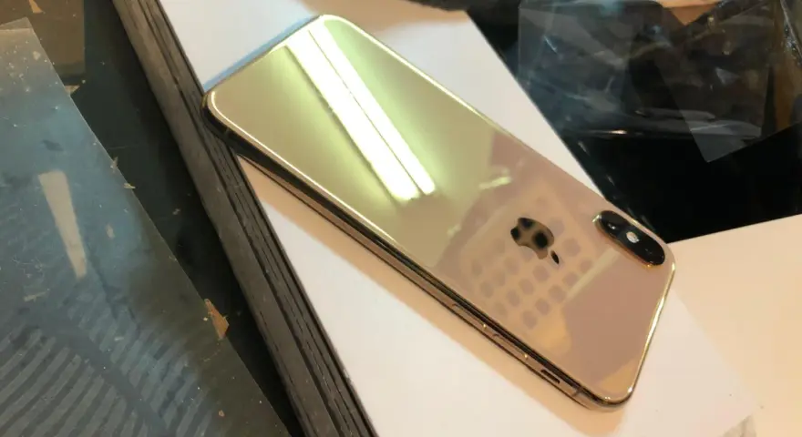 Błyszczący, złoty iPhone X leży na białej powierzchni.
