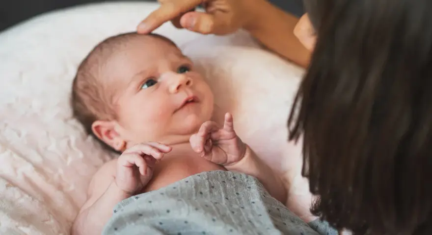 Dłoń rodzica delikatnie dotyka ciemiączka noworodka leżącego na różowej poduszce.
