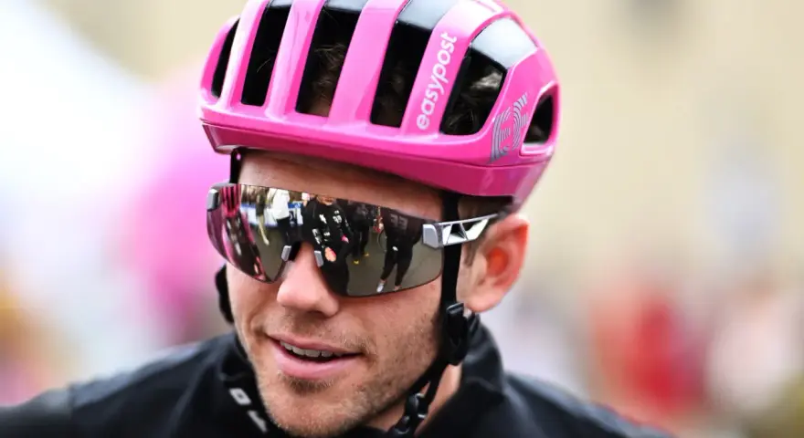 Cyclist Luke Lamperti smiles, wearing a bright pink helmet and reflective sunglasses.
