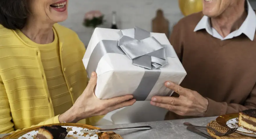 Uśmiechnięta para świętuje 35 rocznicę ślubu, wręczając sobie prezent. Na stole tort i balony.