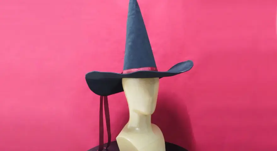 Un mannequin porte un patron chapeau pointu bleu foncé avec un ruban rouge. Deux rubans rouges pendent de chaque côté.