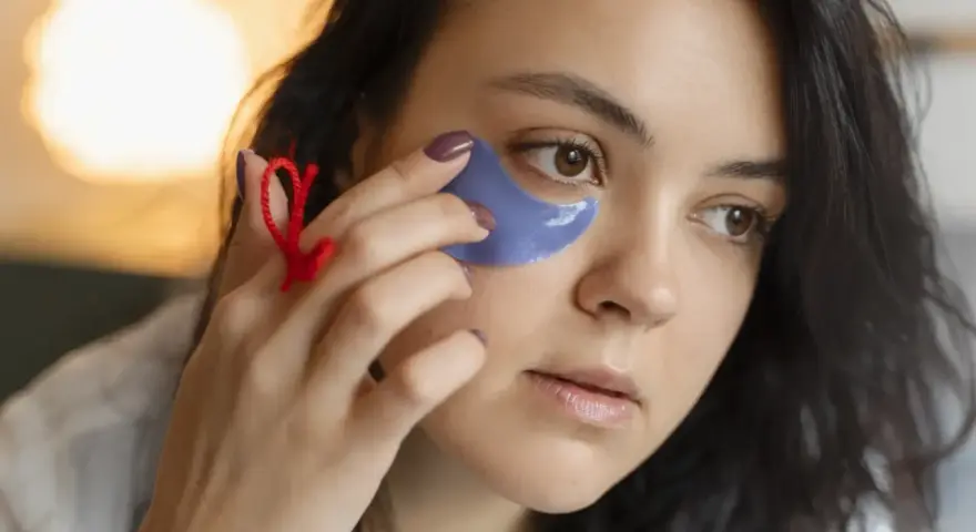 Una mujer se aplica parches de ojos morados. Muestra cómo se ponen los parches de ojos para un cuidado facial.