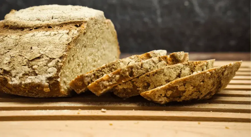 Ein rustikales, selbstgebackenes Brot liegt angeschnitten auf einem Holzbrett. Die Kruste ist knusprig, die Scheiben duften nach Tradition.