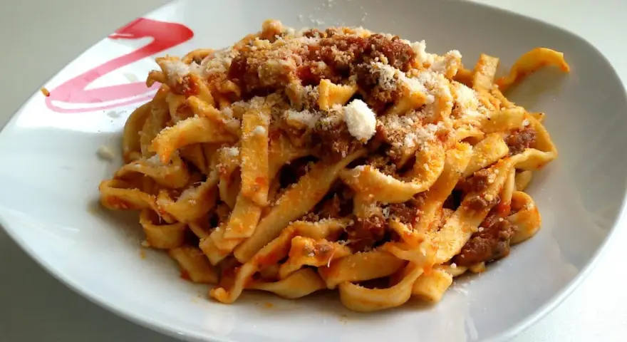 Un piatto invitante di tagliatelle al ragù, condite con abbondante parmigiano grattugiato.