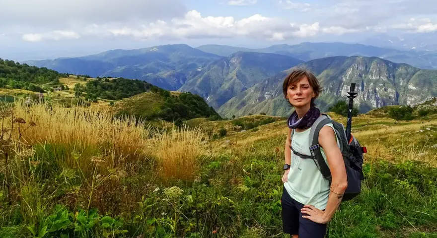 Donna con zaino e bastoncini da trekking ammira il panorama montuoso, un'emozione delle camminate FVG.
