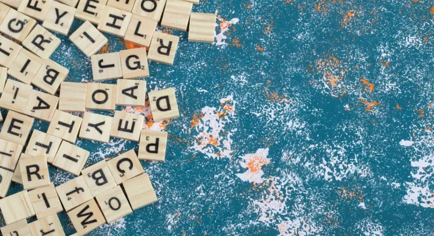 Fichas de letras de madera esparcidas, algunas formando palabras con w, sobre un fondo azul texturizado con salpicaduras blancas y naranjas.
