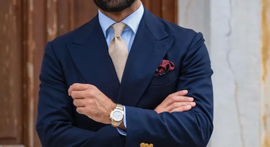 Uomo con abito blu, cravatta beige e fazzoletto bordeaux con un disegno floreale. Il fazzoletto, un dettaglio di stile, aggiunge un tocco di eleganza.