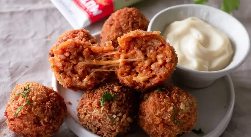 Was sind Arancini? Knusprig frittierte Reisbällchen mit geschmolzenem Käse, serviert mit einer cremigen Dip-Sauce.