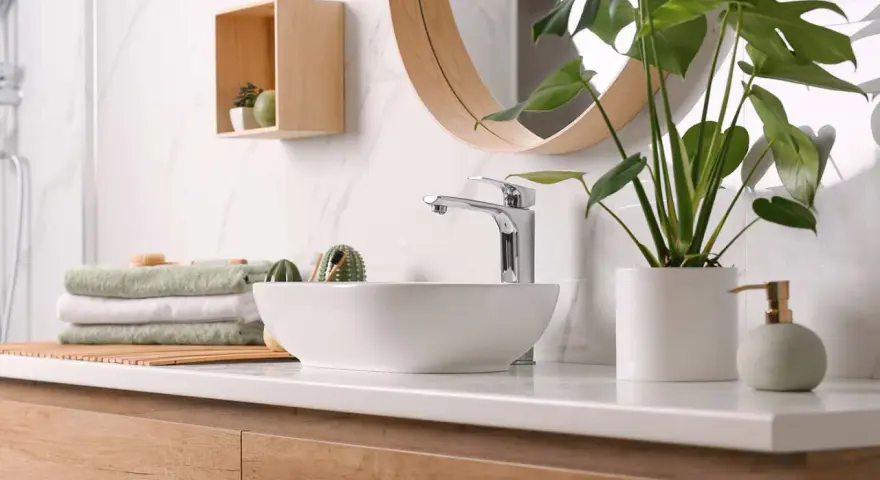Plan de travail de salle de bain moderne avec vasque, robinetterie chromée, serviettes pliées et plante verte. La hauteur du plan de travail est idéale.