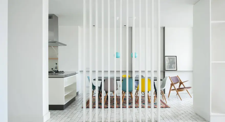 Elegante solución para dividir salón en dos ambientes. Cocina moderna y comedor con sillas de colores, separados por una celosía blanca.