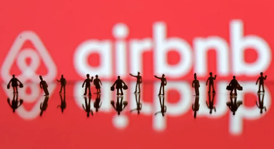 Małe figurki ludzi na tle logo Airbnb. Zastanawiasz się airbnb co to? To platforma do rezerwacji noclegów.