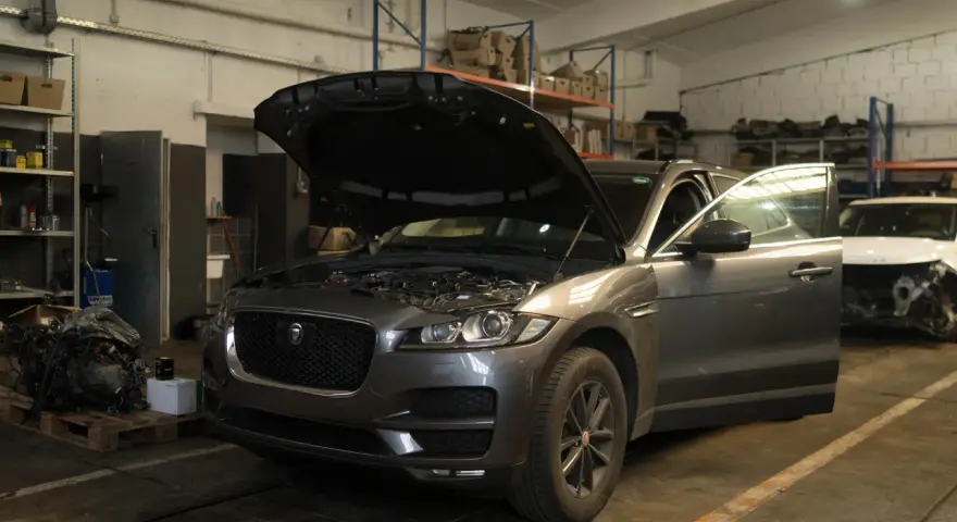 Grauer Jaguar XE mit geöffneter Motorhaube und Tür in einer Werkstatt, bereit für Reparaturen wegen Jaguar XE Probleme.