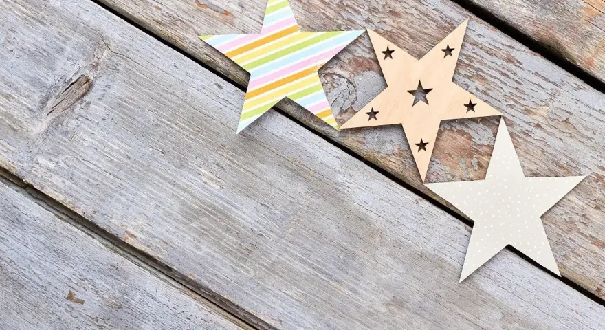 Trzy ozdobne gwiazdy: jedna w kolorowe paski, druga drewniana z wyciętymi gwiazdkami, trzecia w kropki. Piękny rysunek gwiazd na drewnianym tle.
