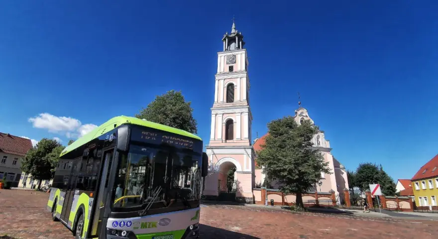 Zielony autobus MZK Chodzież czeka na pasażerów pod wieżą kościoła. Sprawdź mzk chodzież rozkład jazdy i zaplanuj podróż!