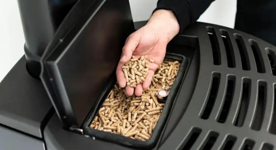 Ręka wsypuje pellet do zasobnika pieca. Dobre opinie o piecach na pellet i drewno to klucz do wyboru ekologicznego ogrzewania.