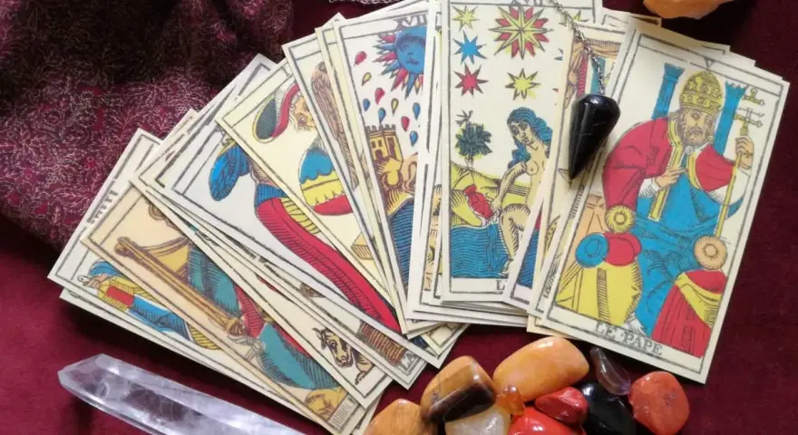 Cartas de tarot psicológico, un péndulo y cristales dispuestos sobre una tela burdeos.