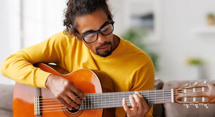 Mann mit Brille hält eine Gitarre und spielt darauf.