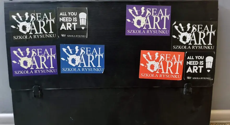 Czarna walizka na prace plastyczne ozdobiona naklejkami "SEAL ART SZKOŁA RYSUNKU" i "ALL YOU NEED IS ART".