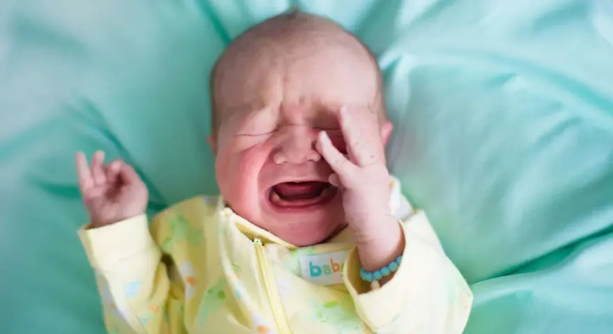 Ein **baby weinen** auf einem türkisfarbenen Tuch, mit geschlossenen Augen und einer Hand vor dem Gesicht.