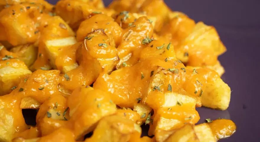 Patatas bravas crujientes cubiertas con una salsa naranja cremosa y hierbas picadas.
